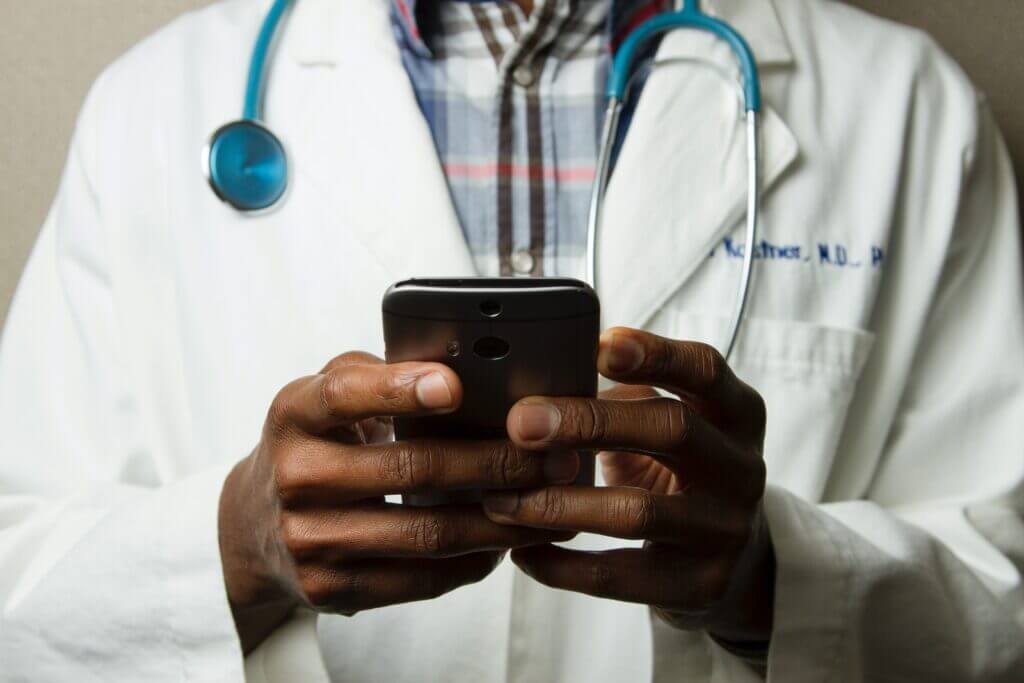 doctor working on healthcare app on his smartphone - healthcare software development services - multishoring