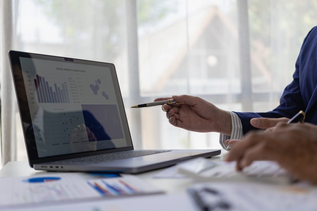 Close-up of a business team sitting at a desk in front of a laptop with a financial infographic and financial document of a startup company brainstorming a new project in a coffee shop.